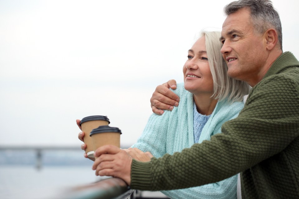 Una pareja mayor sonriente tomando un café junto al mar